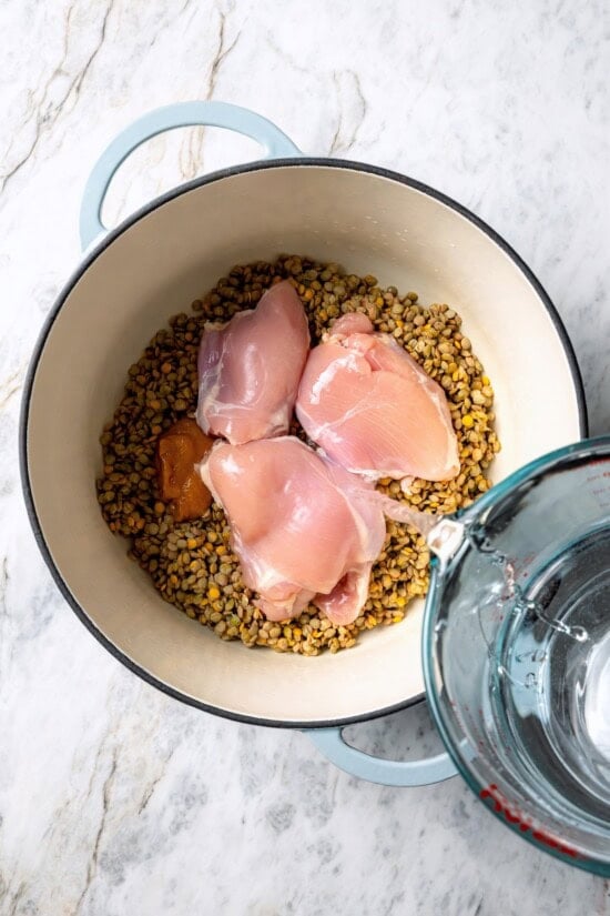 This chicken lentil soup is hearty, flavorful, and easy to make. It’s a nourishing, protein-packed meal perfect for cold days. Pouring water into pot with lentils and raw chicken.