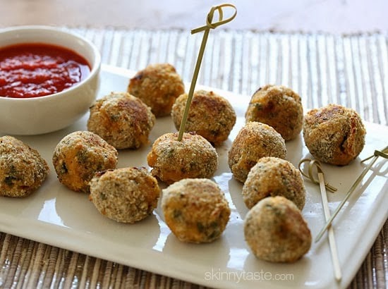 A plate of cooked mini spinach and sausage arancini balls with a bowl of marinara sauce