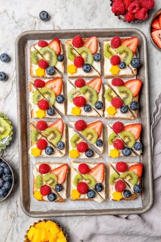 This easy fruit pizza is made with a lightened-up sugar cookie crust and topped with fluffy cream cheese frosting and colorful fresh fruit! Overhead view of sugar cookie fruit pizza on sheet pan