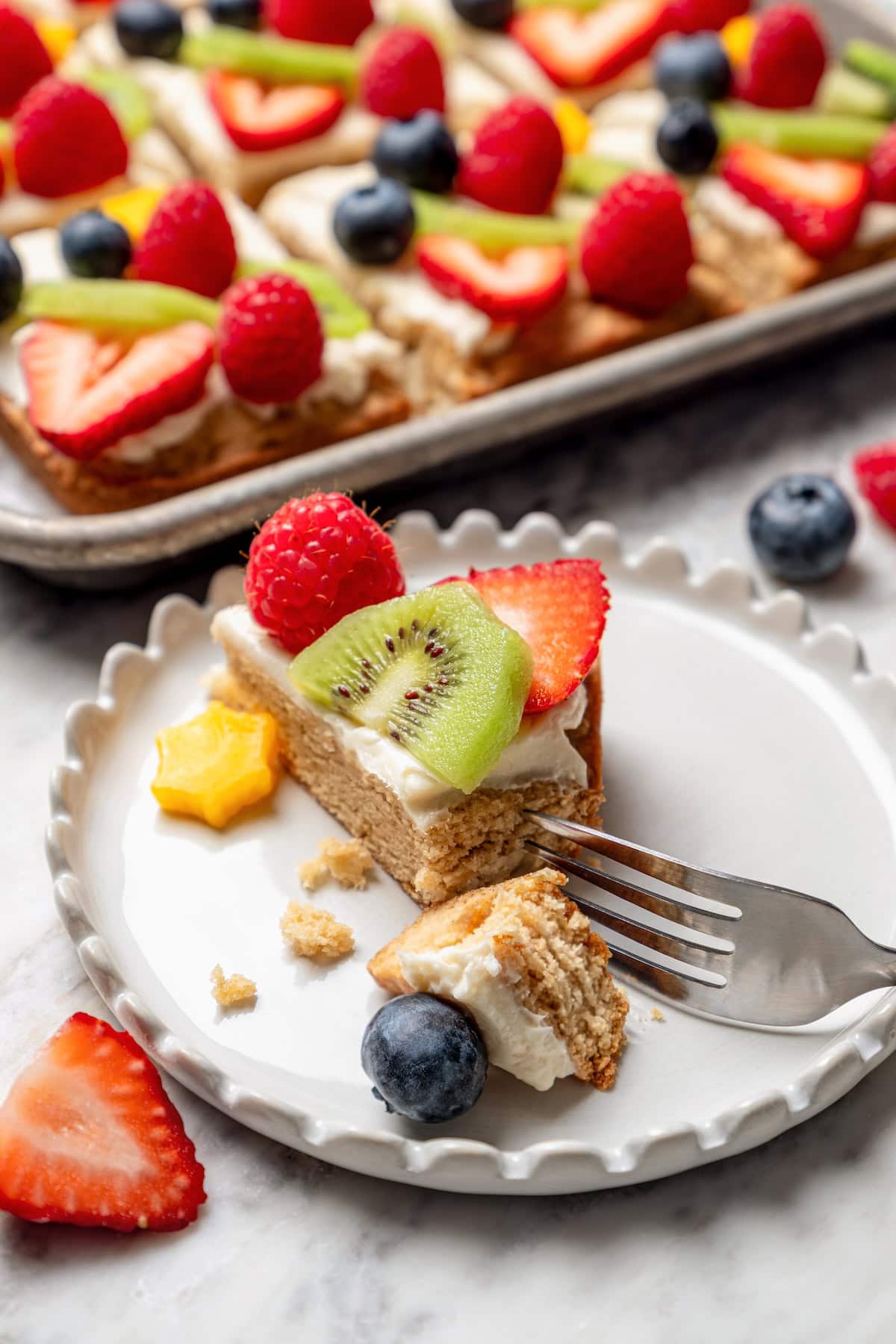 This easy fruit pizza is made with a lightened-up sugar cookie crust and topped with fluffy cream cheese frosting and colorful fresh fruit! Fruit pizza on plate with tip cut off with fork
