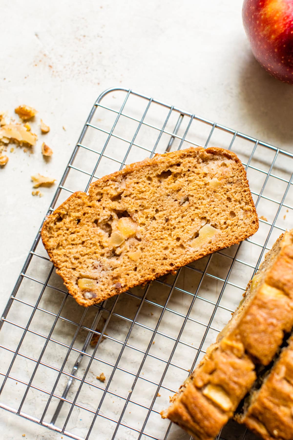 Moist apple bread recipe made with homemade applesauce, fresh apple chunks, spices, and walnuts in every bite. It's easy and so delicious! Overhead view of a spice of apple bread on a wire rack.