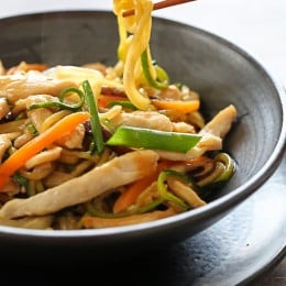 Chopsticks holding a zucchini noodle over a bowl of Chicken zoodle lo mein.