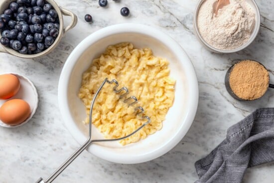This blueberry banana bread is a lighter twist on a classic that’s perfect for breakfast, snacking, or anytime you have ripe bananas to use! Potato masher in bowl with mashed banana.