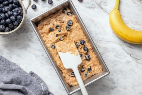 This blueberry banana bread is a lighter twist on a classic that’s perfect for breakfast, snacking, or anytime you have ripe bananas to use! Spreading blueberry banana bread batter into pan.