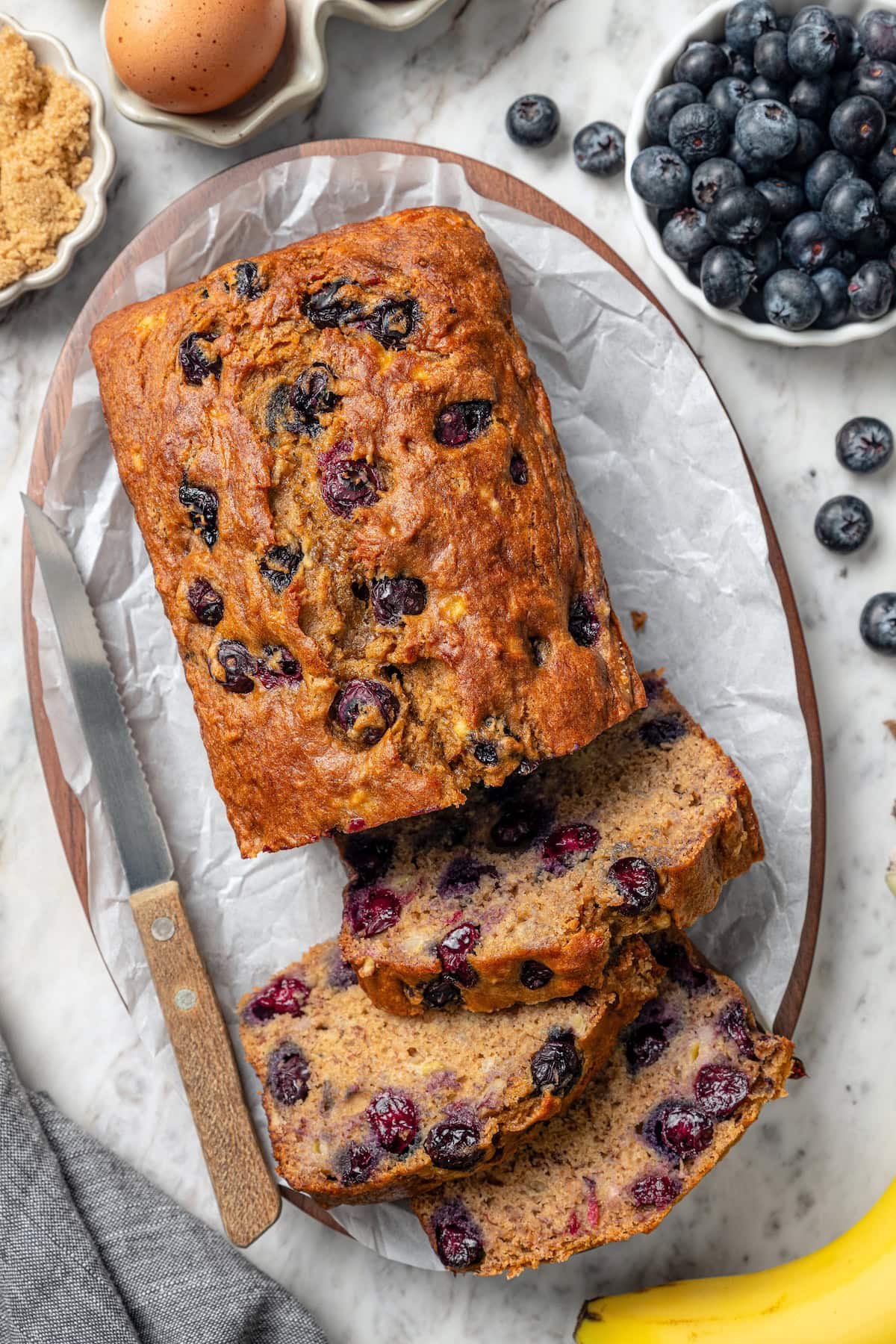 This blueberry banana bread is a lighter twist on a classic that’s perfect for breakfast, snacking, or anytime you have ripe bananas to use! Loaf of blueberry banana bread with 3 slices cut.