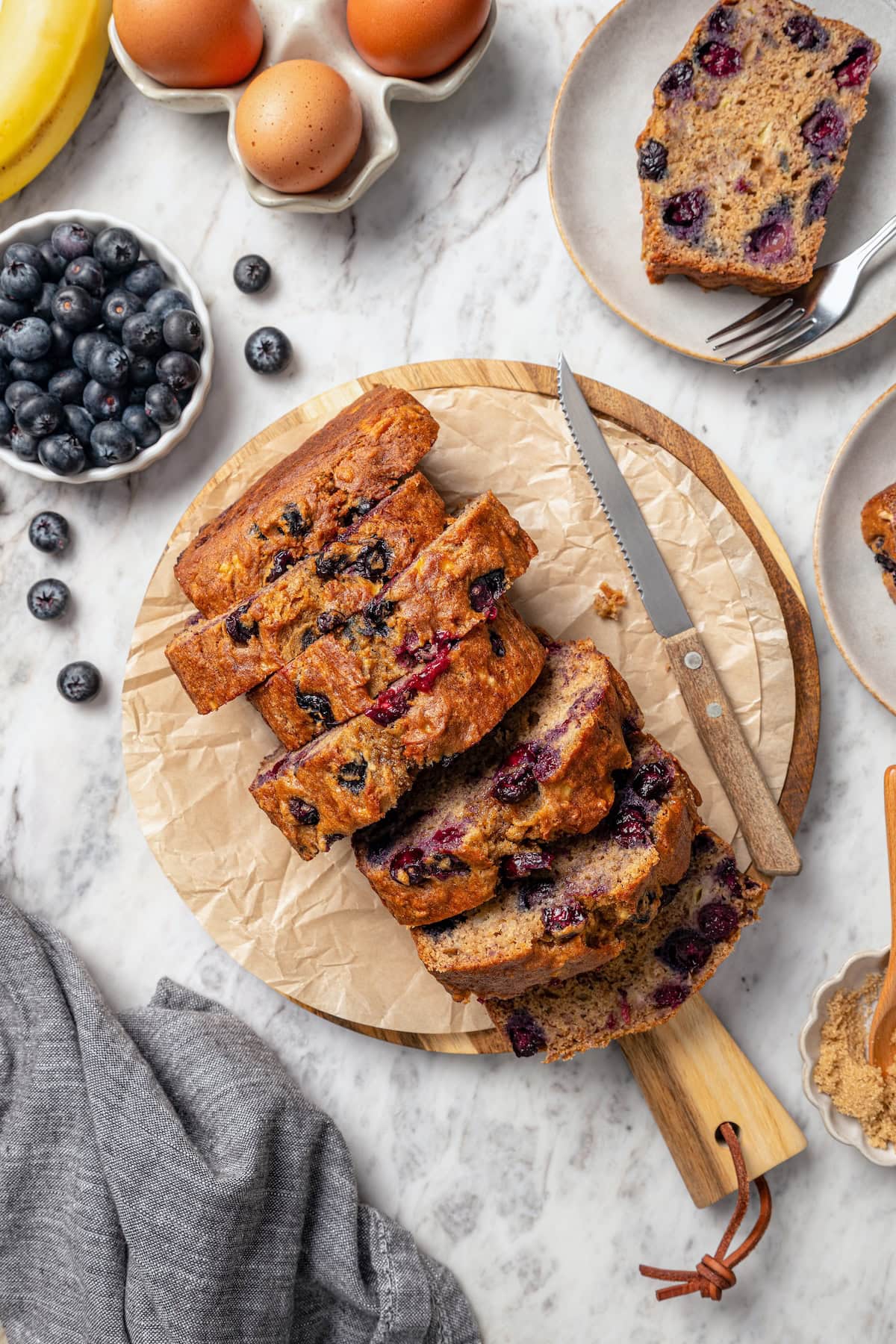 This blueberry banana bread is a lighter twist on a classic that’s perfect for breakfast, snacking, or anytime you have ripe bananas to use! Sliced loaf of blueberry banana bread on cutting board.