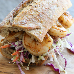 A shrimp po' boy sandwich on a wooden cutting board.