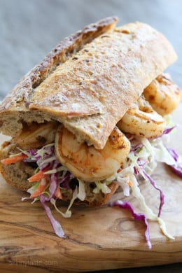 A shrimp po' boy sandwich on a wooden cutting board.