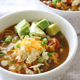 A bowl of pumpkin chili topped with shredded cheese and avocado