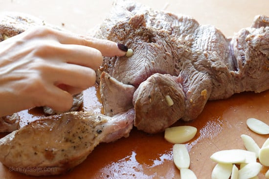 The best Instant Pot Carnitas recipe! Make juicy Mexican pulled pork in the pressure cooker for tacos, burrito bowls, taco salads, and more. A hand presses garlic slivers into small holes cut in the side of a browned pork shoulder.