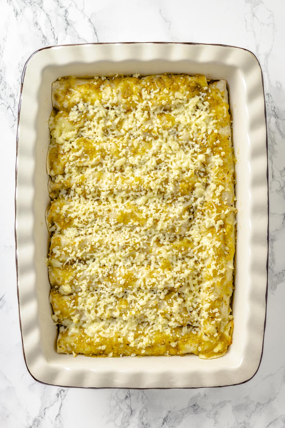 These Chicken Enchiladas Verdes (aka Green Enchiladas) are made with white corn tortillas, salsa verde, chicken breast, and queso fresco. A casserole dish of chicken green enchiladas