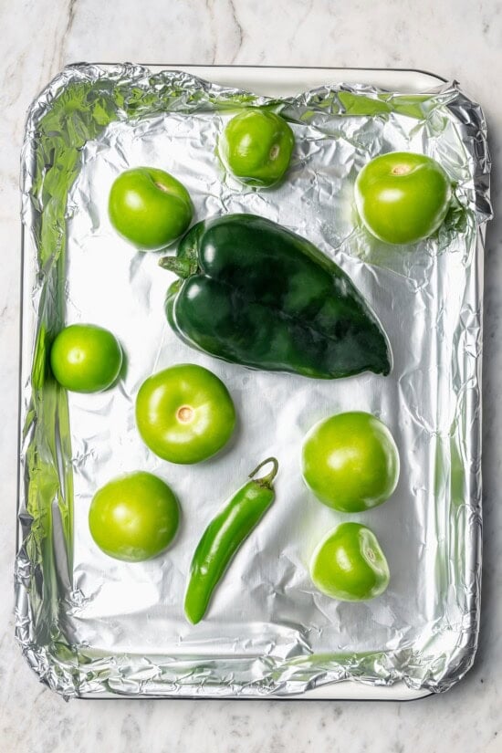 Roasting the tomatillos and peppers first makes this homemade salsa verde recipe extra delicious. Easy to make and better than store-bought! Overhead view of peppers and tomatillos on foil lined pan
