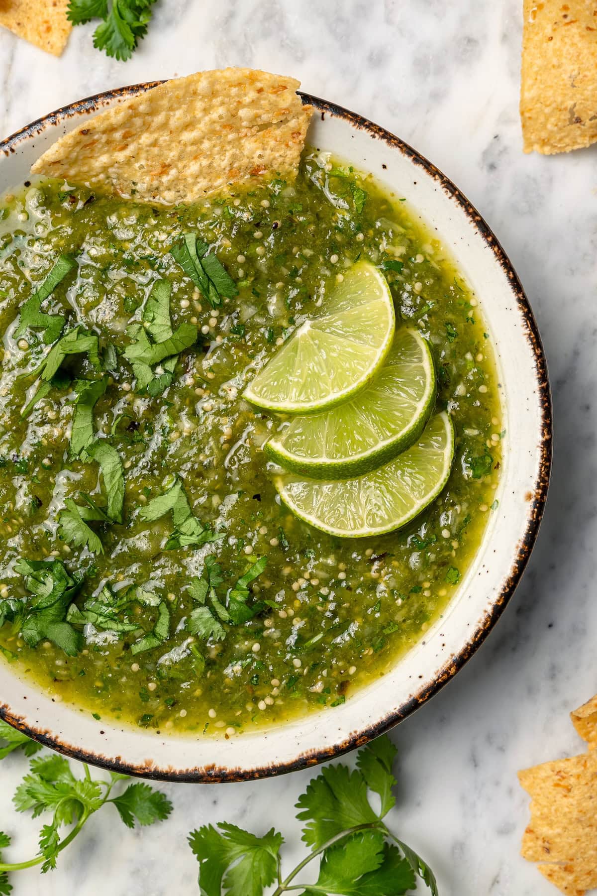 Roasting the tomatillos and peppers first makes this homemade salsa verde recipe extra delicious. Easy to make and better than store-bought! Bowl of salsa verde with 3 lime wedges and chip