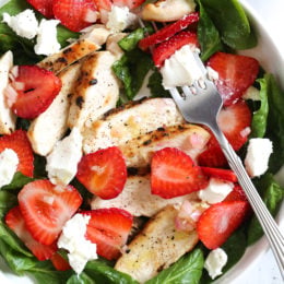 Overhead view of a strawberry chicken salad with spinach and goat cheese in a bowl with a fork.