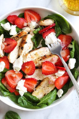 Overhead view of a strawberry chicken salad with spinach and goat cheese in a bowl with a fork.