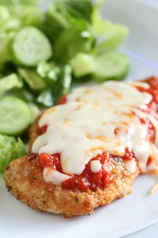 Quick and cheesy air fryer chicken parmesan is an easy, weeknight-friendly dinner. A lighter spin on the classic Italian chicken dish! Chicken parmesan next to salad on a plate.