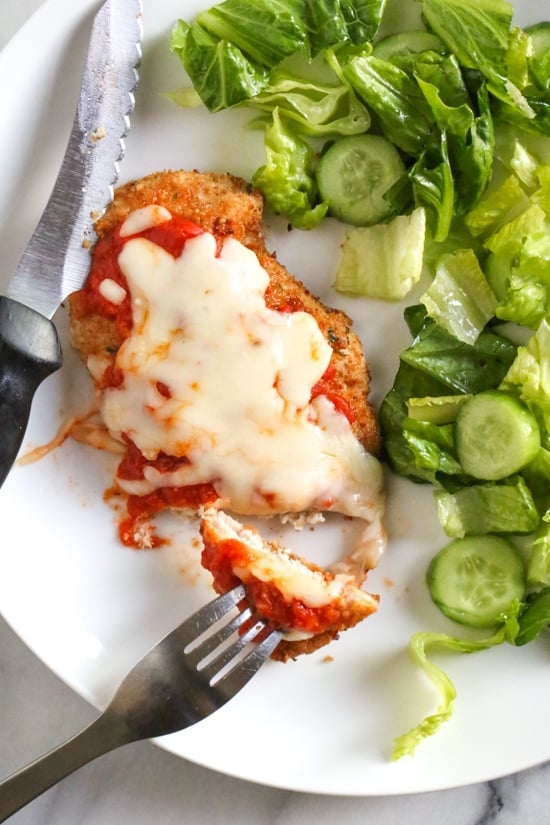 Quick and cheesy air fryer chicken parmesan is an easy, weeknight-friendly dinner. A lighter spin on the classic Italian chicken dish! Overhead view of chicken parmesan next to salad on a plate.