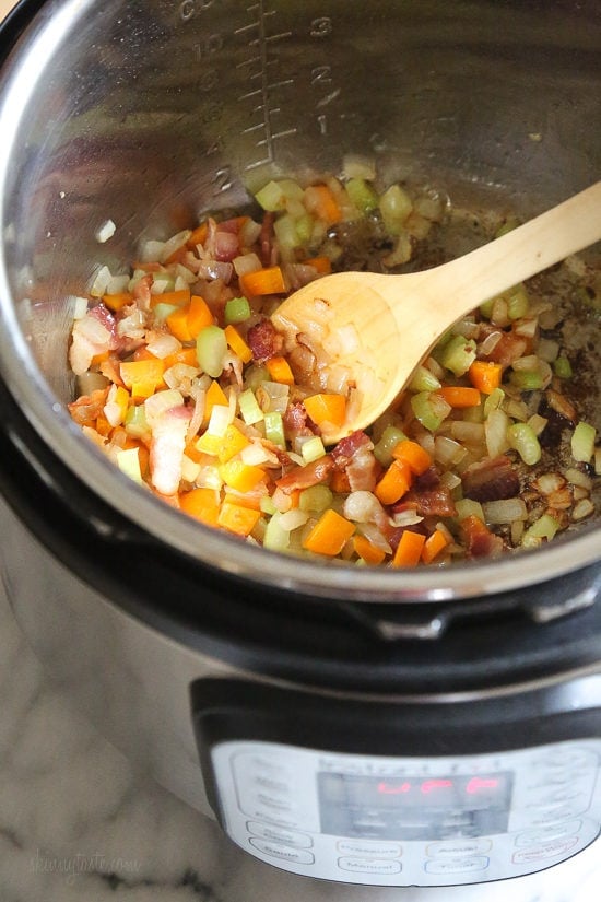 Instant Pot Bolognese sauce is full of flavor and ready in one hour! See how easy it is to make a classic meat sauce in your pressure cooker. Diced veggies sauteing inside the Instant Pot next to a wooden spoon.
