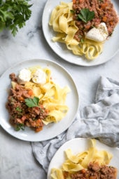 Overhead view of three plates of pasta bolognese garnished with parsley and cheese.