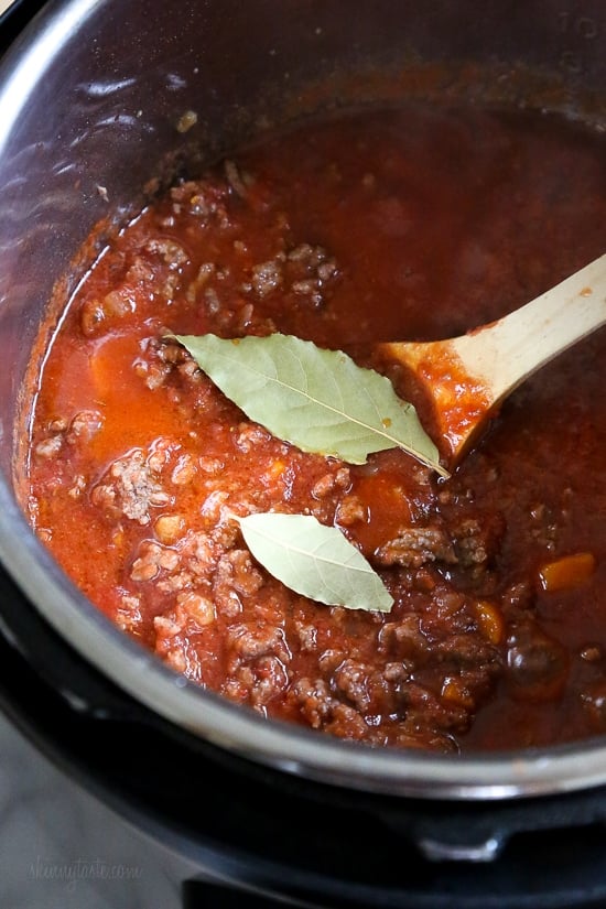 Instant Pot Bolognese sauce is full of flavor and ready in one hour! See how easy it is to make a classic meat sauce in your pressure cooker. Instant Pot bolognese sauce inside the pressure cooker, with bay leaves next to a wooden spoon.