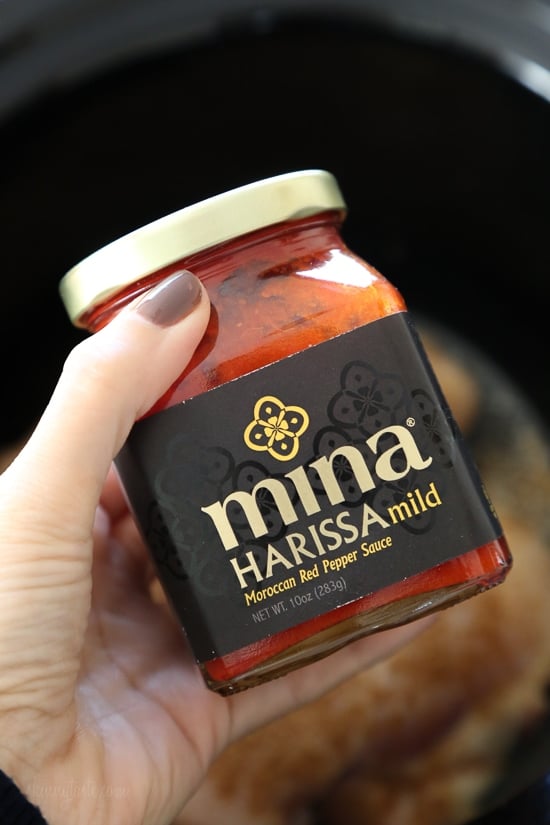 An easy harissa chicken recipe made in the slow cooker or Instant Pot, made with just 5 ingredients! Perfect for bowls, meal prep, and more. A hand holding a jar of Mina harissa paste.