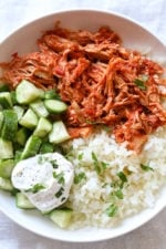 Overhead view of a harissa chicken bowl with yogurt sauce, cucumber, and rice.