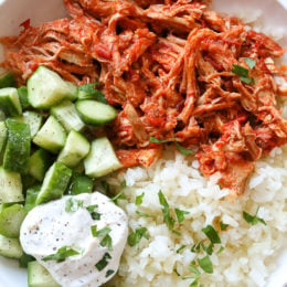Overhead view of a harissa chicken bowl with yogurt sauce, cucumber, and rice.