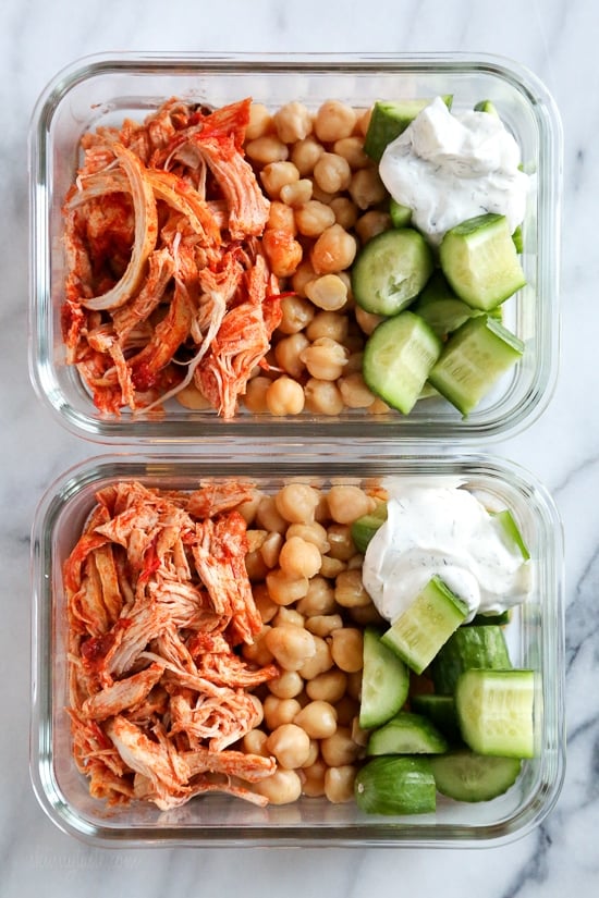 An easy harissa chicken recipe made in the slow cooker or Instant Pot, made with just 5 ingredients! Perfect for bowls, meal prep, and more. Overhead view of harissa chicken with yogurt sauce, cucumber, and rice in two meal prep containers.