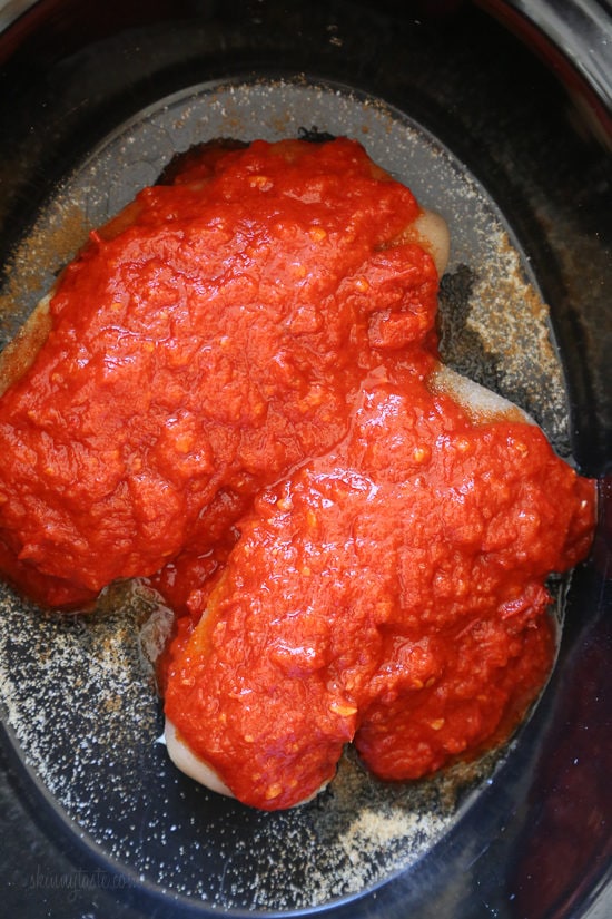 An easy harissa chicken recipe made in the slow cooker or Instant Pot, made with just 5 ingredients! Perfect for bowls, meal prep, and more. Overhead view of harissa sauce added to chicken breasts inside the slow cooker.