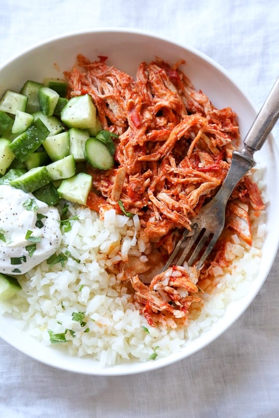 An easy harissa chicken recipe made in the slow cooker or Instant Pot, made with just 5 ingredients! Perfect for bowls, meal prep, and more. Overhead view of slow cooker harissa chicken with yogurt sauce, cucumber, and rice.
