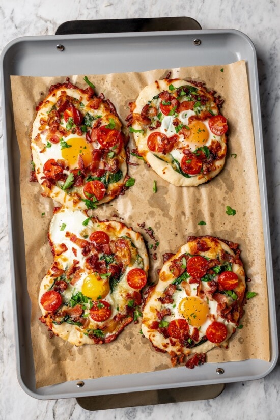 This easy breakfast pizza features a crispy yogurt crust topped with eggs, cheese, spinach and bacon for a savory protein-packed meal. 4 persona breakfast pizzas on parchment-lined pan.