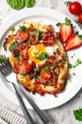 Breakfast pizza with egg, bacon, tomatoes, and spinach on plate.