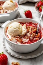 Scoop of vanilla ice cream on top of strawberry crisp in bowl