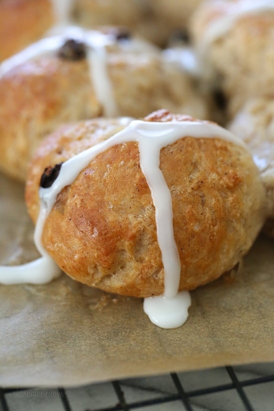 Make soft homemade hot cross buns without yeast, filled with spice, raisins, and finished with icing. Easy to bake in the oven or air fryer! Close up of a hot cross bun topped with icing on a parchment-lined rack.
