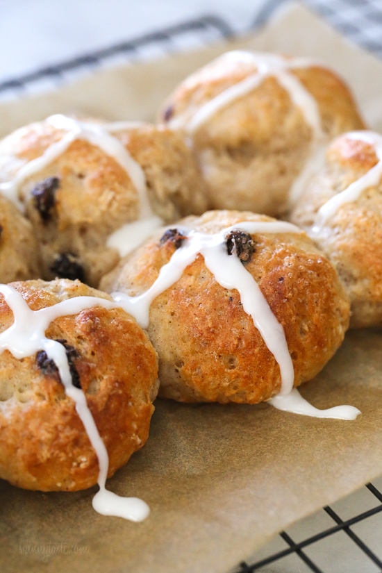 Make soft homemade hot cross buns without yeast, filled with spice, raisins, and finished with icing. Easy to bake in the oven or air fryer! Close up of hot cross buns topped with icing on a parchment-lined rack.