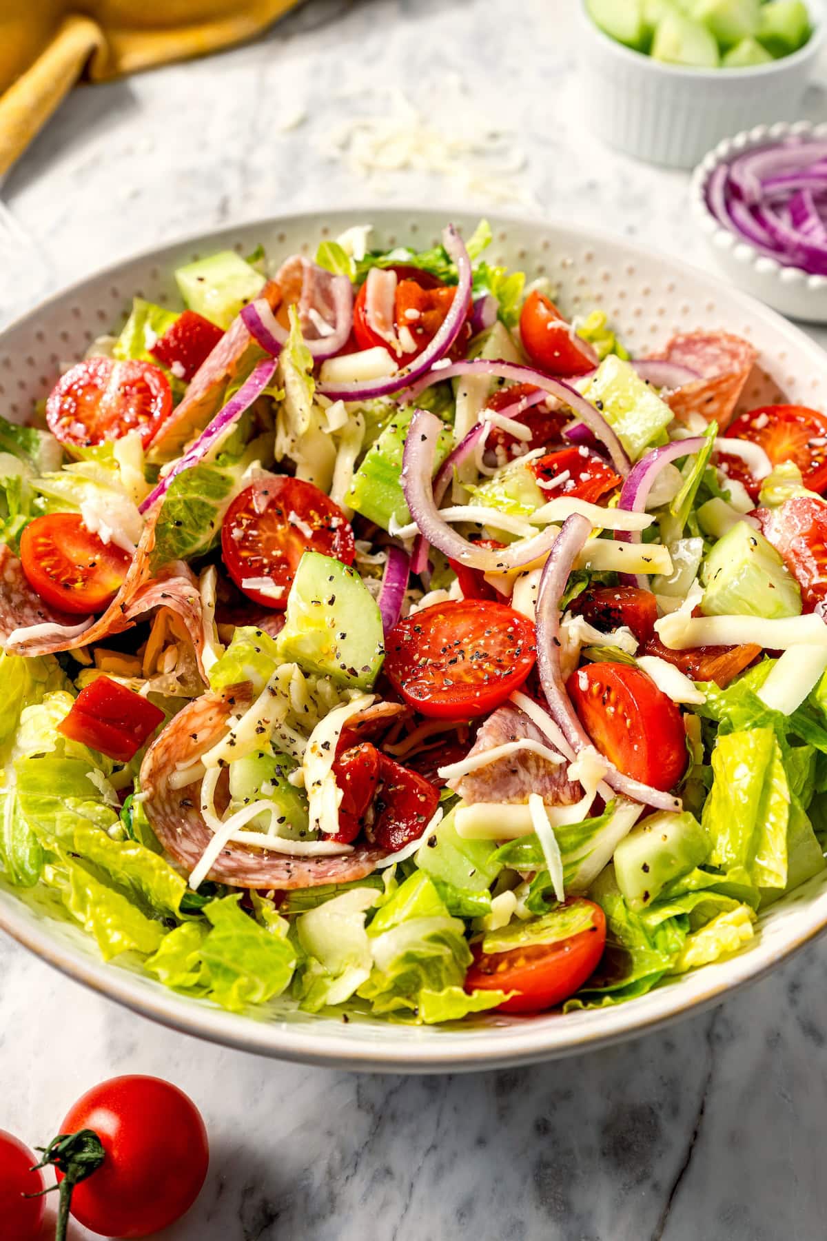 This easy Italian chopped salad pairs crisp romaine with salami, mozzarella, roasted red pepper, and veggies in red wine vinaigrette. Delish! Italian chopped salad in large serving bowl.