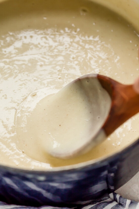 Cozy and comforting, this Potato Leek Soup is an easy soup recipe the whole family will love. It's rich and creamy, without any heavy cream! Wooden spoon stirring potato leek soup in pot