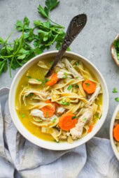 Overhead view of a bowl of chicken noodle soup next to fresh parsley.