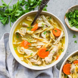 Overhead view of a bowl of chicken noodle soup next to fresh parsley and a second bowl of soup.