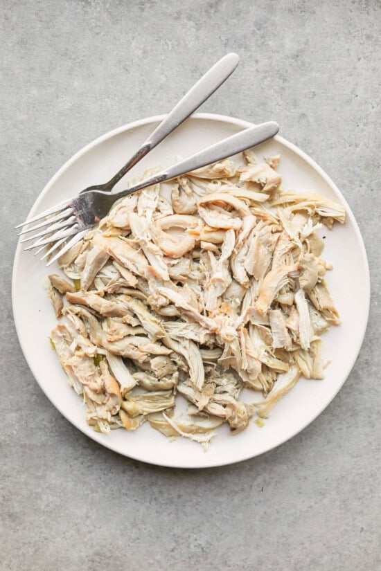 Shredded chicken next to two forks on a plate.