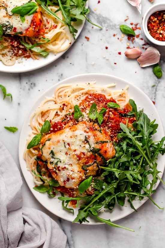 This quick and easy Instant Pot Chicken Parmesan is ready in minutes, with no breading or frying. Perfect for busy weeknights! Overhead view of two plates of Instant Pot chicken parm with spaghetti noodles and greens