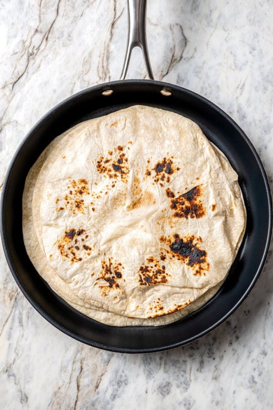 These easy freezer breakfast burritos are a delicious, protein-packed way to start the day with scrambled eggs, veggies, bacon and cheese. Tortillas in pan