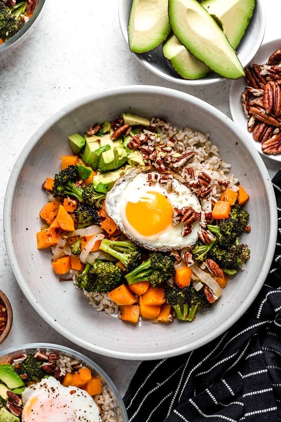This easy Buddha bowl pairs a brown rice base with roasted broccoli, butternut squash, creamy avocado, fried eggs, and pecans. So delicious! Overhead view of Buddha bowl topped with fried egg and pecans