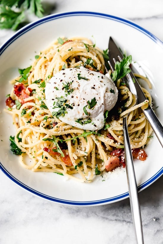 With diced bacon, grated cheese, black pepper, and a poached egg, this Spaghetti Carbonara is simple yet elegant. A bowl of spaghetti carbonara topped with a poached egg