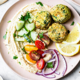 Overhead view of falafel served with hummus and a tomato cucumber salad on a plate.