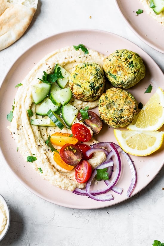 Overhead view of falafel served with hummus and a tomato cucumber salad on a plate.