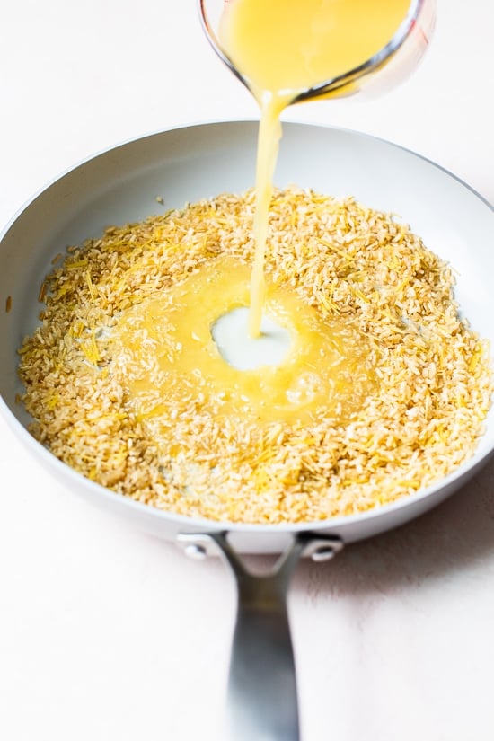This homemade Rice-a-Roni style rice pilaf is made with toasted pasta, brown rice, and broth for an easy, buttery, family-friendly side dish. Pouring broth into skillet of rice and pasta for pilaf.