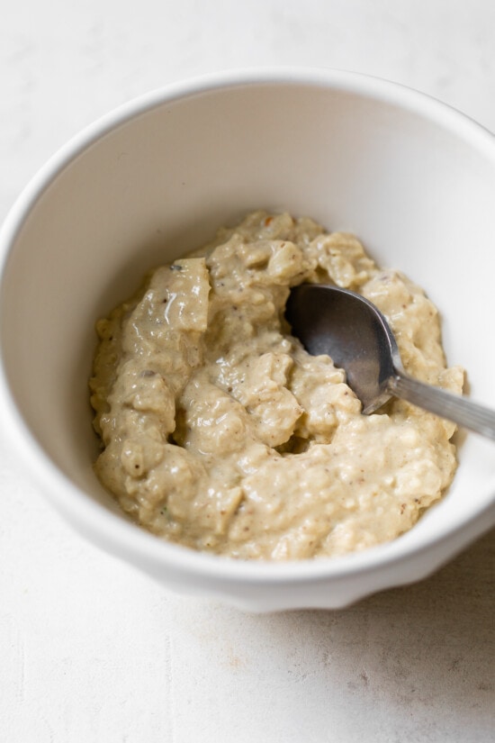 This authentic baba ganoush recipe is smoky, smooth, lemony and garlicky. It's a healthy dip that's easy to make and so delicious! Mashed eggplant in bowl with spoon.