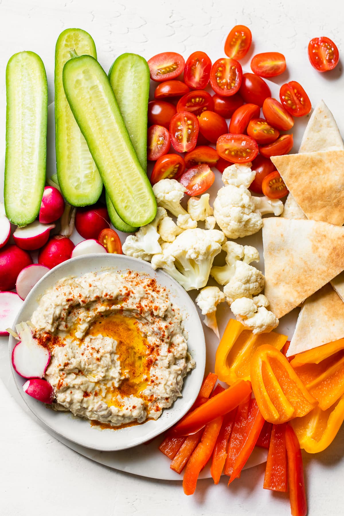 This authentic baba ganoush recipe is smoky, smooth, lemony and garlicky. It's a healthy dip that's easy to make and so delicious! Baba ganoush in bowl on platter with pita bread and vegetables.