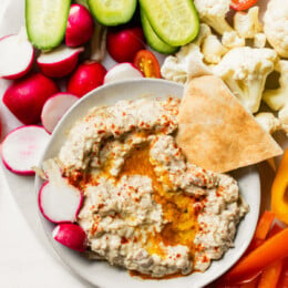 Dipping pita triangle in bowl of baba ganoush.